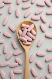 Photo of Vitamin pills and wooden spoon on light grey background, top view. Health supplement