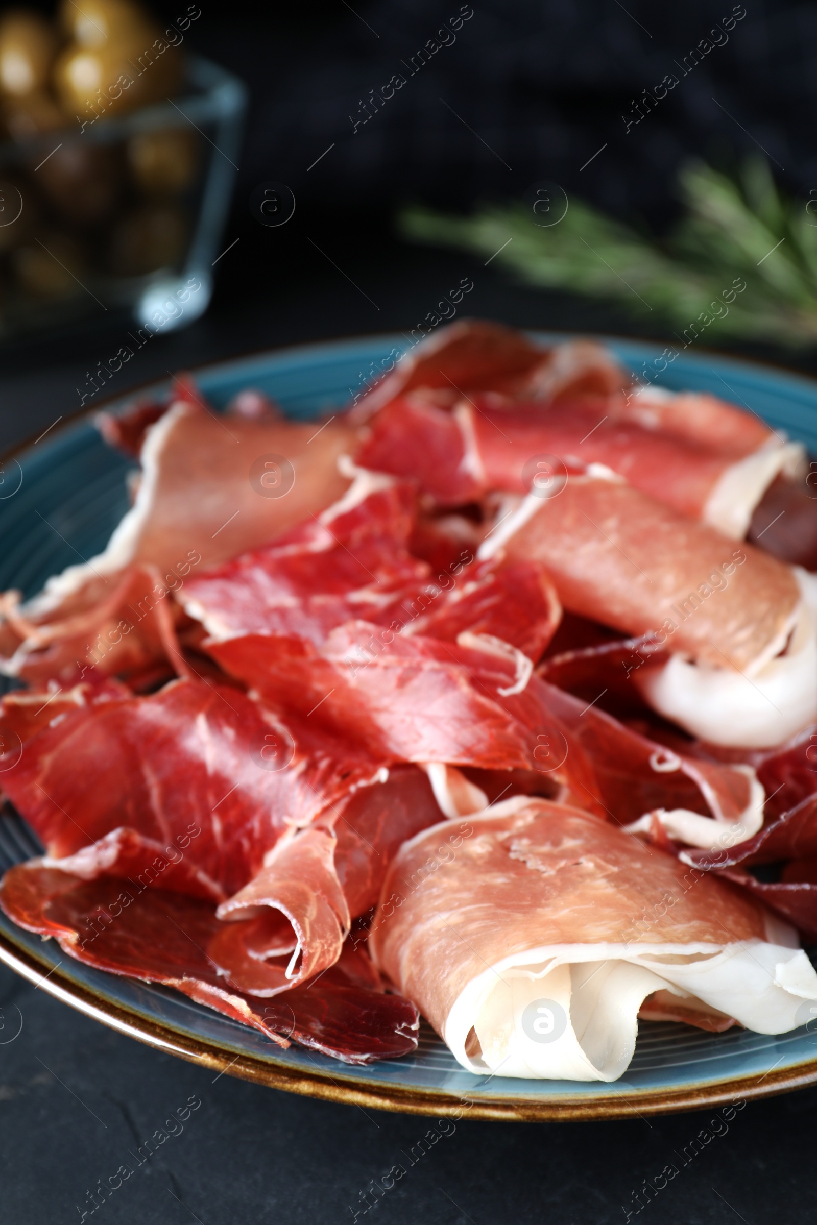 Photo of Tasty fresh prosciutto on black table, closeup