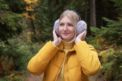 Photo of Young beautiful woman wearing warm earmuffs in forest