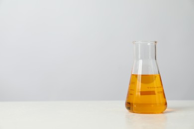 Photo of Glass flask with yellow oil on white table, space for text