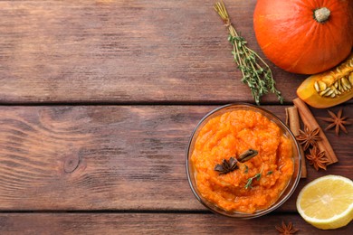 Photo of Bowl of delicious pumpkin jam and ingredients on wooden table, flat lay. Space for text