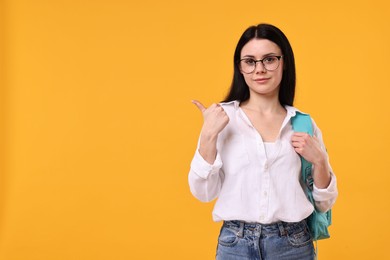 Photo of Student in glasses pointing at something on yellow background. Space for text