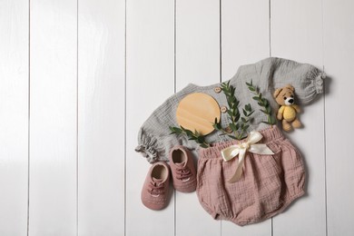 Photo of Flat lay composition with children's clothes, shoes and toy on white wooden table. Space for text
