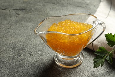 Photo of Fresh pike caviar in gravy boat and parsley on grey table, closeup