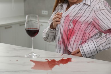 Photo of Woman with spilled wine over her shirt and marble table in kitchen, closeup