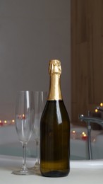 Photo of Bottle of champagne, glasses and burning candles near jacuzzi in bathroom