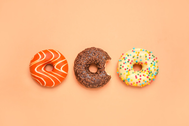 Photo of Delicious glazed donuts on orange background, flat lay