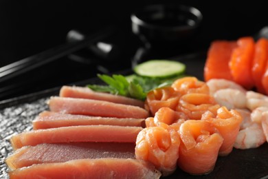 Photo of Delicious sashimi set of salmon, tuna and shrimps served with parsley and cucumber on black serving board, closeup