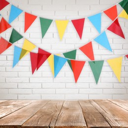 Image of Empty wooden table and decorative bunting flags hanging on white brick wall