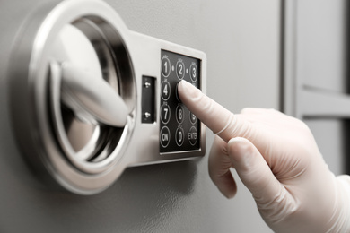 Photo of Woman in gloves entering code on keypad of modern safe, closeup