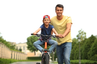 Image of Dad teaching son to ride bicycle outdoors