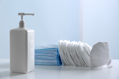 Photo of Hand sanitizer and respiratory masks on table against white background. Protective essentials during COVID-19 pandemic