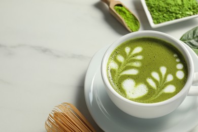 Photo of Delicious matcha latte in cup on white marble table. Space for text