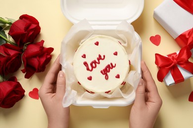 Photo of Woman holding takeaway box with bento cake at beige table, top view. St. Valentine's day surprise