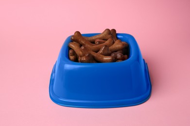 Photo of Blue bowl with bone shaped dog cookies on pink background