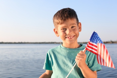 Photo of Cute little boy with American flag near river on sunny day