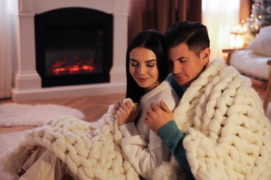Photo of Couple covered in plaid sitting near fireplace at home