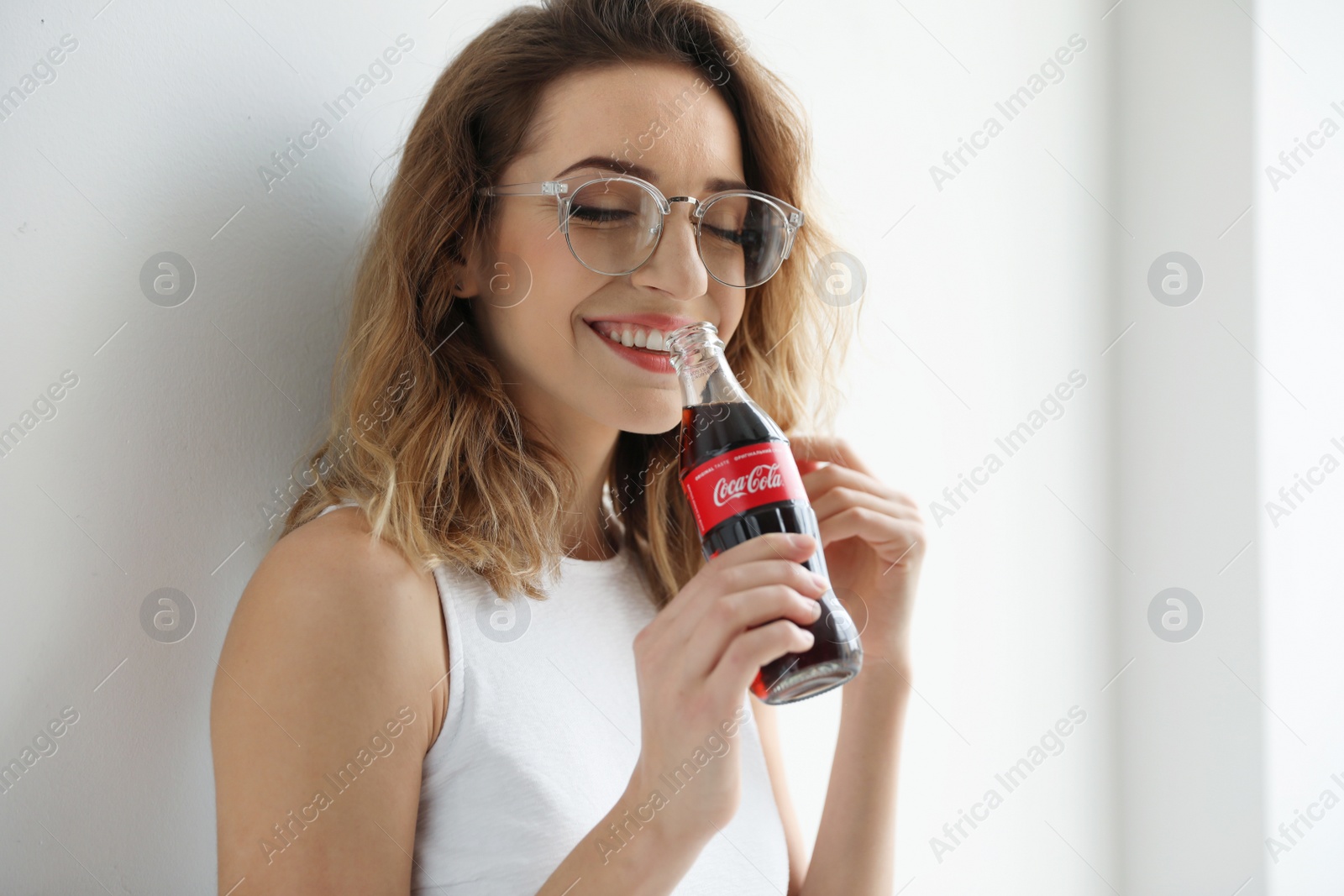 Photo of MYKOLAIV, UKRAINE - NOVEMBER 28, 2018: Young woman with bottle of Coca-Cola indoors