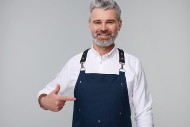 Photo of Happy man pointing at kitchen apron on grey background. Mockup for design