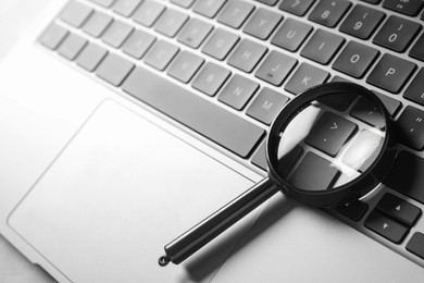 Photo of Magnifying glass and modern laptop on light grey table, closeup