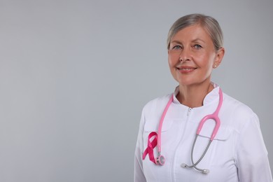 Photo of Doctor with pink ribbon and stethoscope on light grey background, space for text. Breast cancer awareness