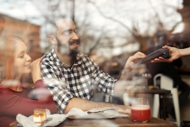 Photo of Man with credit card using payment terminal at restaurant, view through window