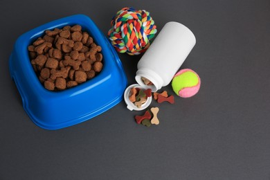 Photo of Bottle with vitamins, toys and dry pet food in bowl on grey background, above view. Space for text