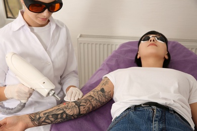 Photo of Young woman undergoing laser tattoo removal procedure in salon