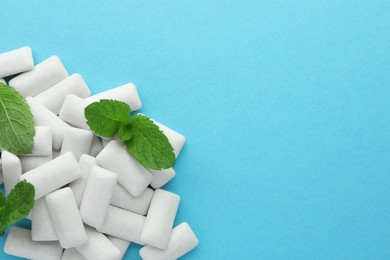 Photo of Pile of tasty white chewing gums and mint leaves on light blue background, top view. Space for text
