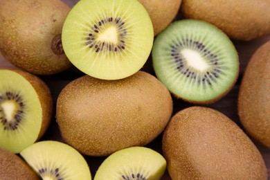 Photo of Many whole and cut fresh kiwis on wooden table, closeup