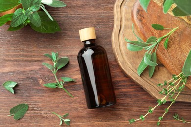 Photo of Bottle of essential oil and fresh herbs on wooden table, flat lay