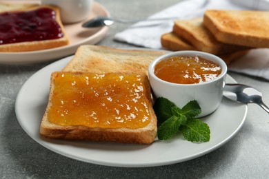 Photo of Delicious toasts served with jam and mint on light grey table, closeup