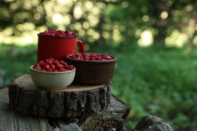 Photo of Dishes with tasty wild strawberries on stump against blurred background, closeup. Space for text