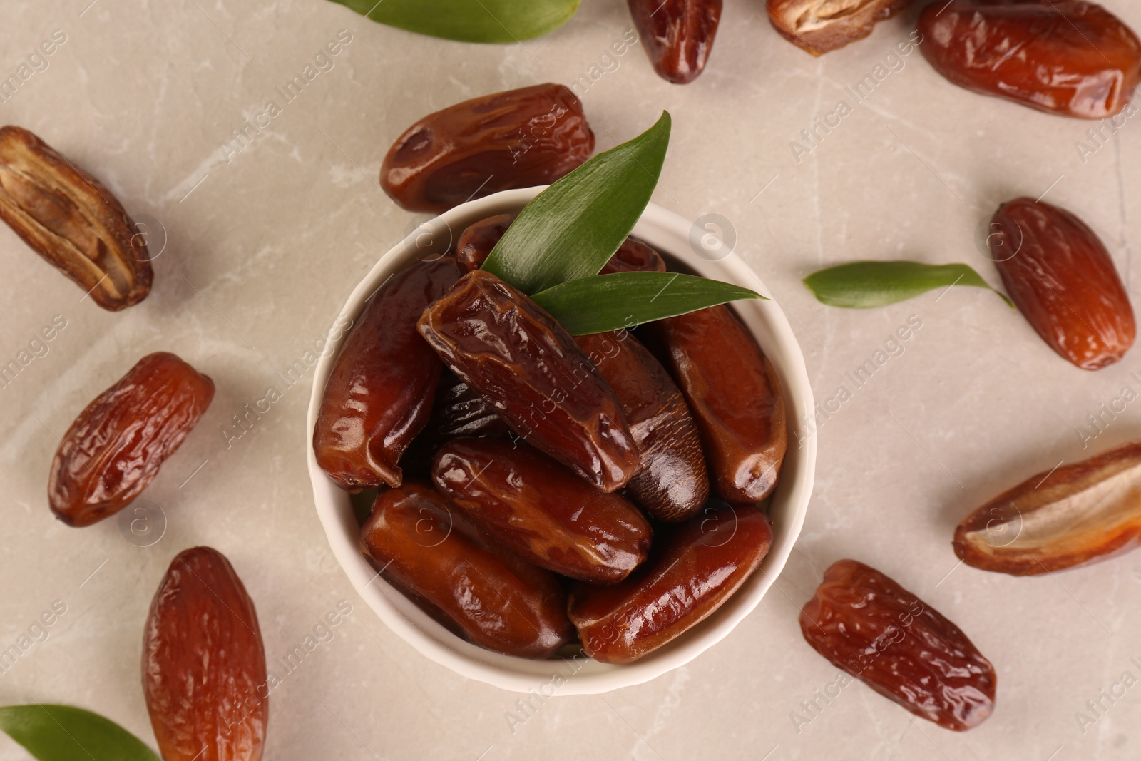 Photo of Tasty sweet dried dates and green leaves on light grey table, flat lay