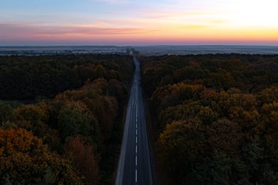 Image of Aerial view of road going through beautiful autumn forest in evening