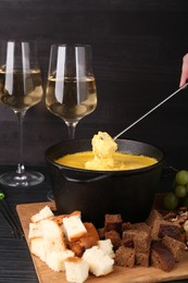 Photo of Woman dipping piece of bread into fondue pot with melted cheese at black wooden table, closeup