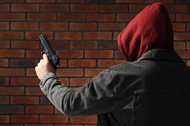 Photo of Dangerous criminal with gun near brick wall, back view. Armed robbery