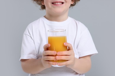 Photo of Cute little boy with glass of fresh juice on light gray background, closeup