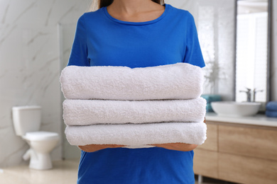 Photo of Woman holding fresh towels in bathroom, closeup