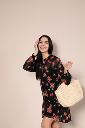 Photo of Young woman wearing floral print dress with straw bag on beige background