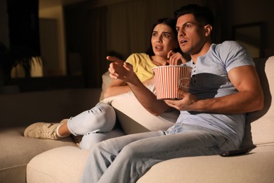 Photo of Couple watching movie with popcorn on sofa at night