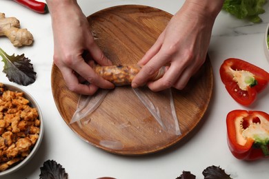 Photo of Woman making tasty spring roll at white marble table, top view