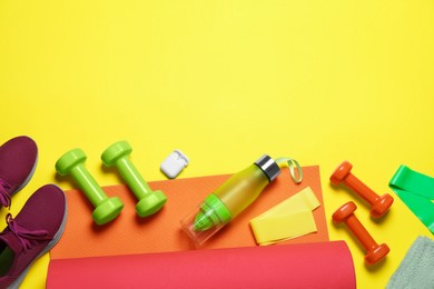 Photo of Exercise mat, dumbbells, bottle of water, wireless earphones, fitness elastic bands and shoes on yellow background, flat lay. Space for text