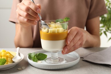 Photo of Woman eating delicious panna cotta with mango at table, closeup