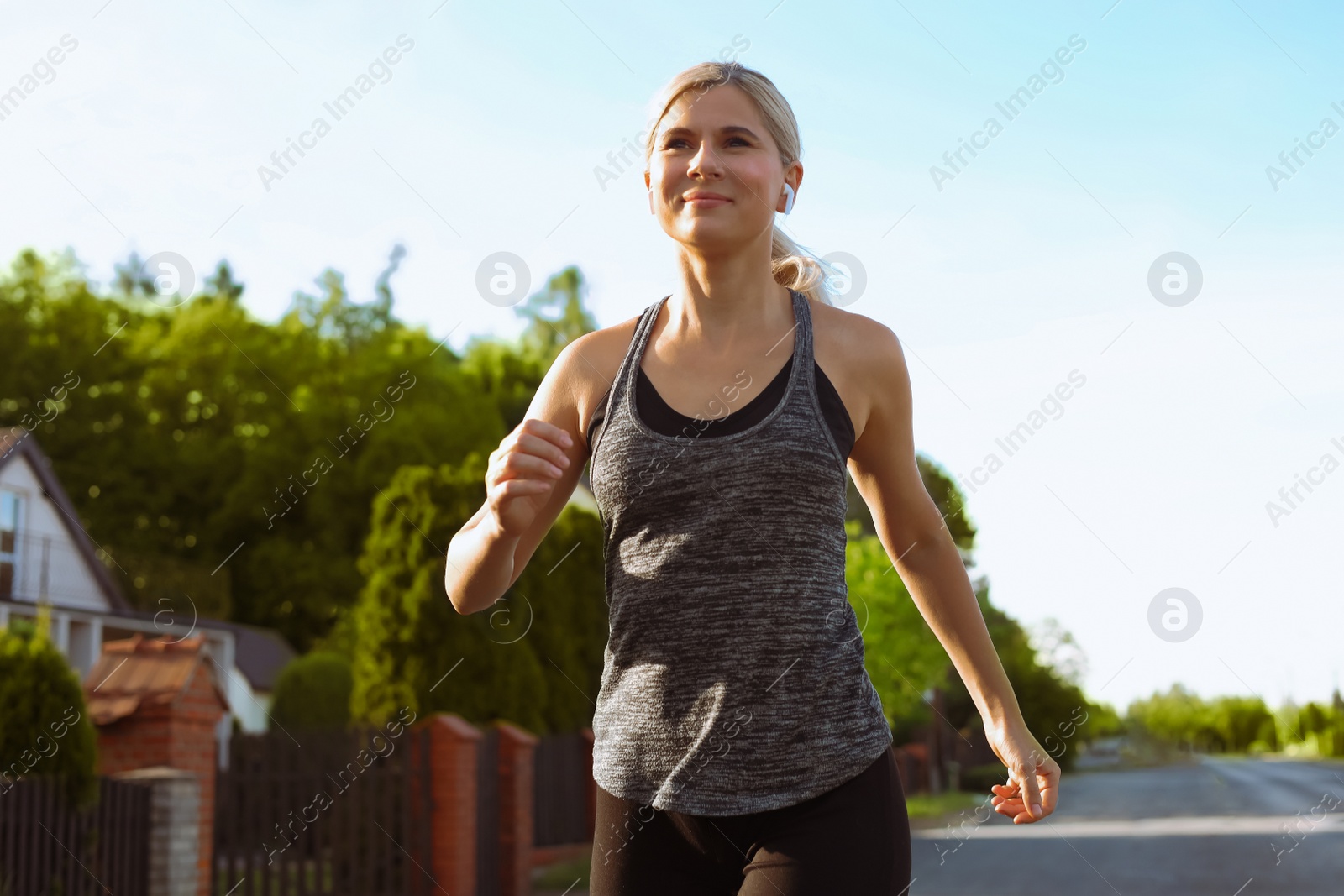 Photo of Woman with wireless earphones jogging around neighborhood in morning