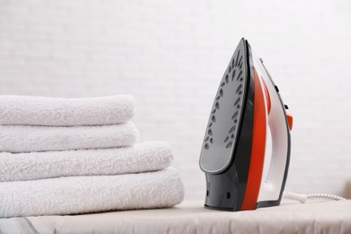 Photo of New modern iron and clean towels on board against light background. Laundry day