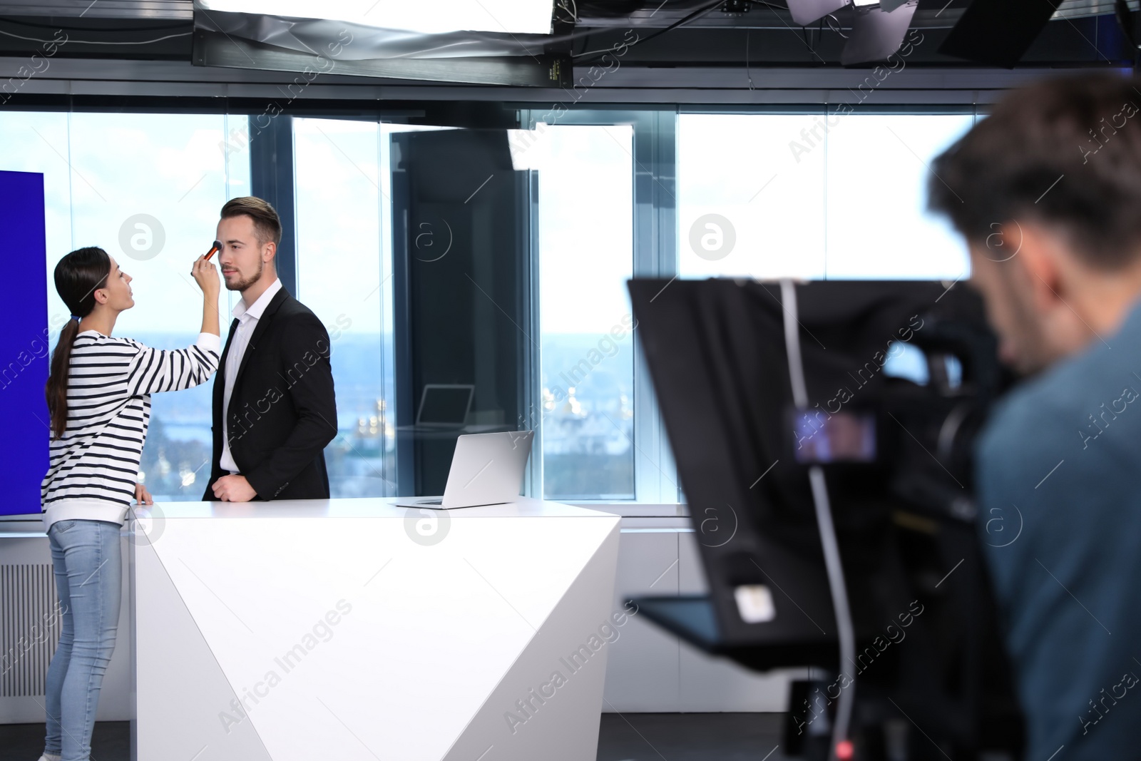 Photo of Presenter, makeup artist and video camera operator working in studio. News broadcasting
