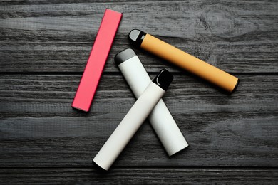 Photo of Different disposable electronic cigarettes on black wooden table, flat lay. Smoking alternative