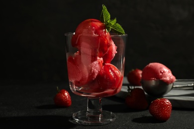 Photo of Delicious strawberry ice cream in dessert bowl on black table against dark background