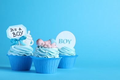 Photo of Beautifully decorated baby shower cupcakes with cream and boy toppers on light blue background. Space for text